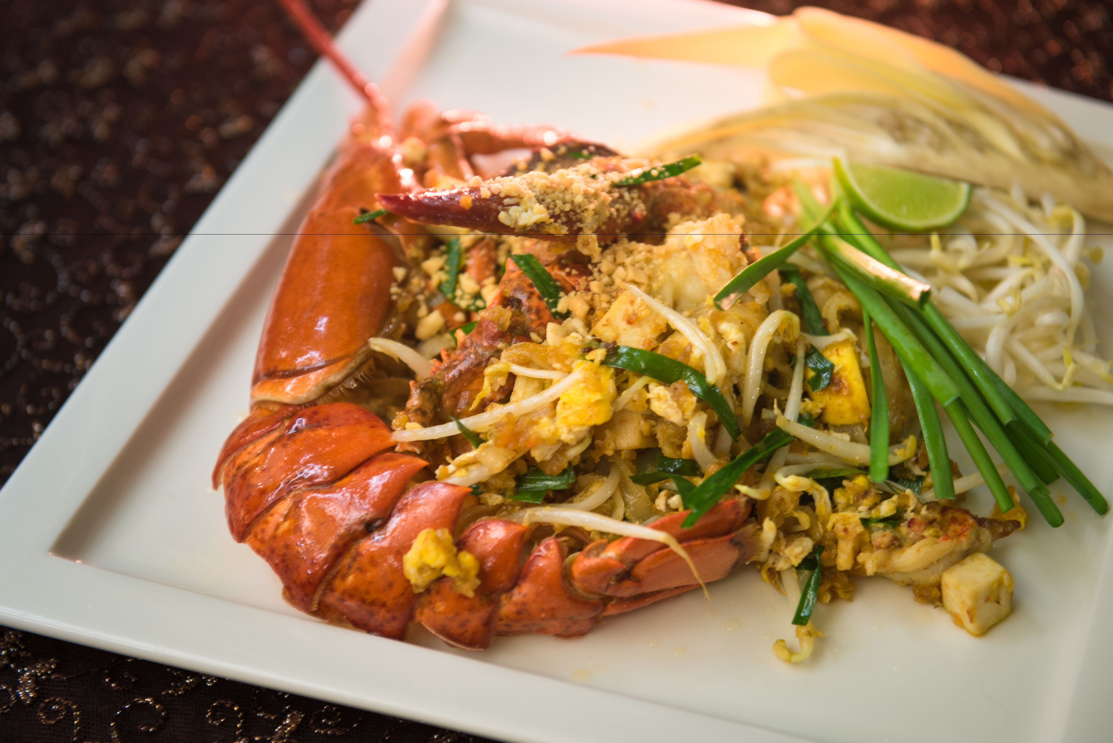 A plate of Pad Thai with a whole lobster, bean sprouts, lime, and green onions.