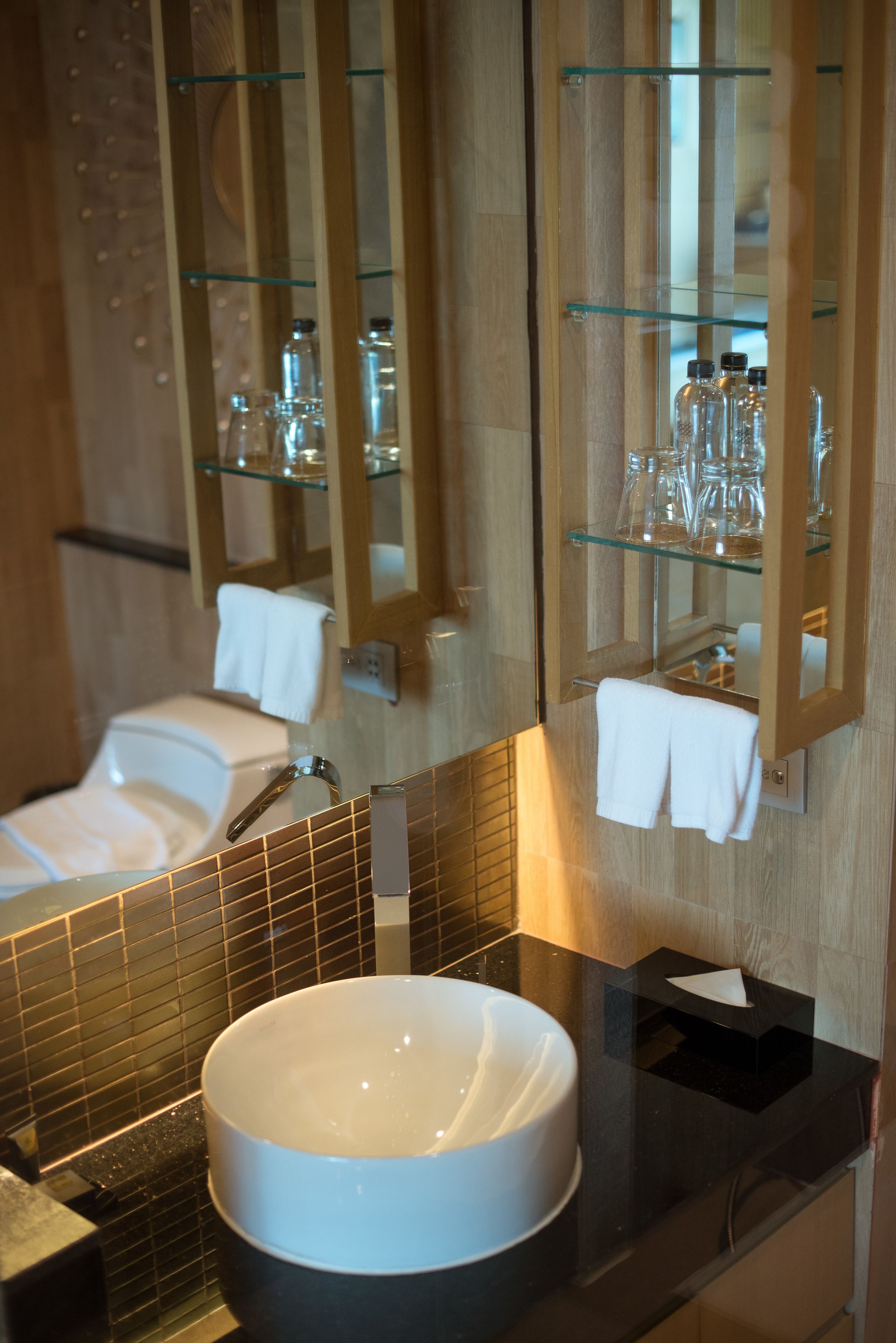 Un baño con un lavabo redondo, una repisa de vidrio con artículos de tocador y un espejo que refleja la habitación.