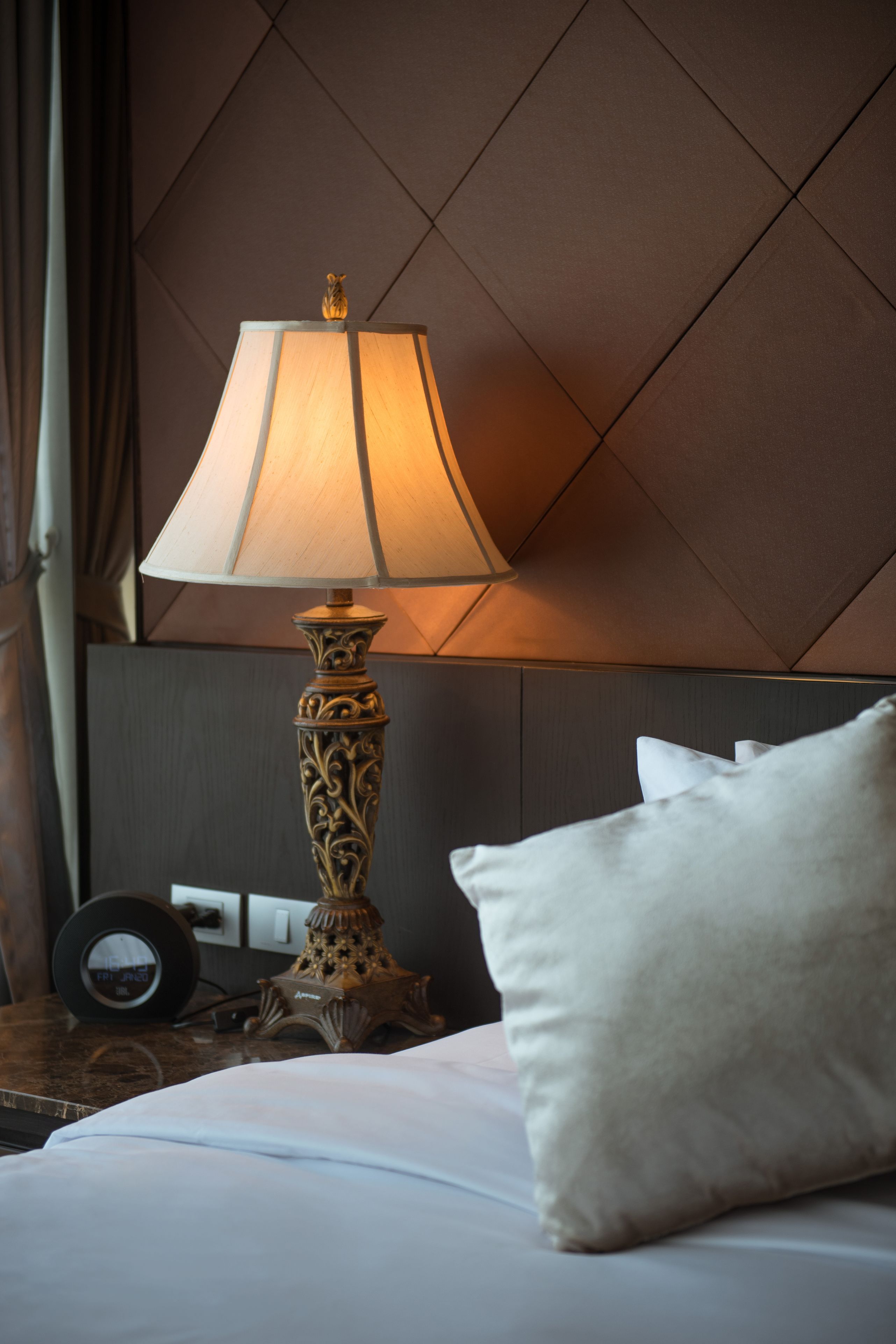 A neatly made bed with a white pillow and a decorative lamp with a beige shade.