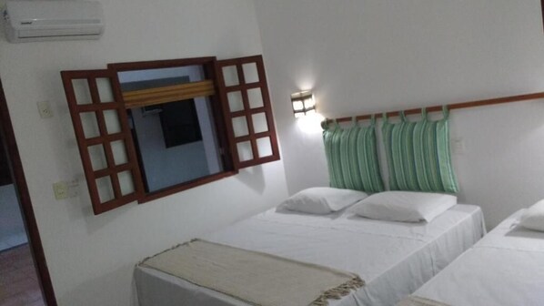 Una habitación con dos camas, una ventana de madera, aire acondicionado en la pared y una lámpara de pared.
