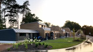 A row of modern, single-story buildings with flat roofs, likely residential or small commercial units, surrounded by a well-maintained lawn and trees.