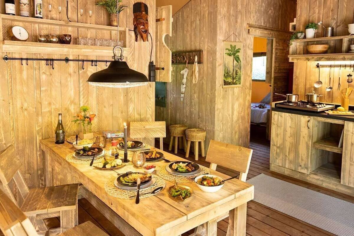 A rustic wooden dining area with a table set for a meal, a hanging light fixture, and a kitchen area with wooden cabinets and utensils.