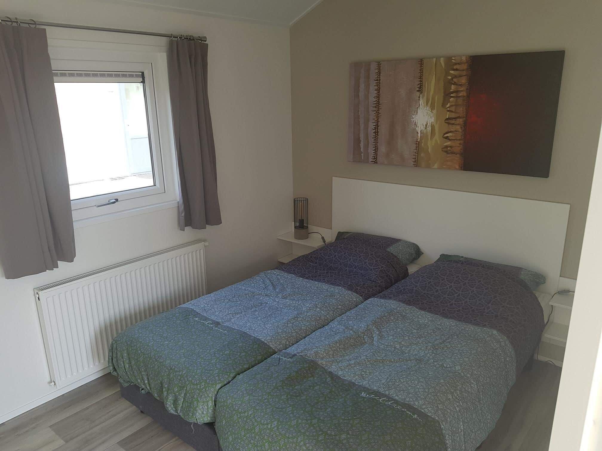 Un dormitorio con dos camas, una ventana con cortinas, un radiador y un cuadro en la pared.