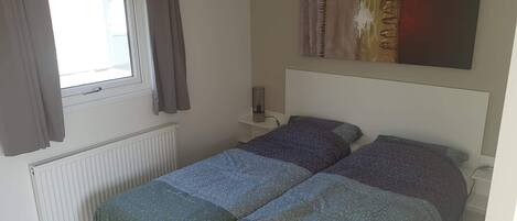 Un dormitorio con dos camas, una ventana con cortinas, un radiador y un cuadro en la pared.