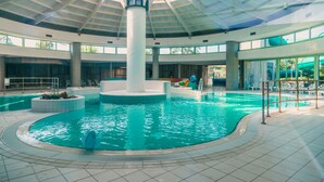 An indoor swimming pool with a central column, tiled floor, and a view of the outside.