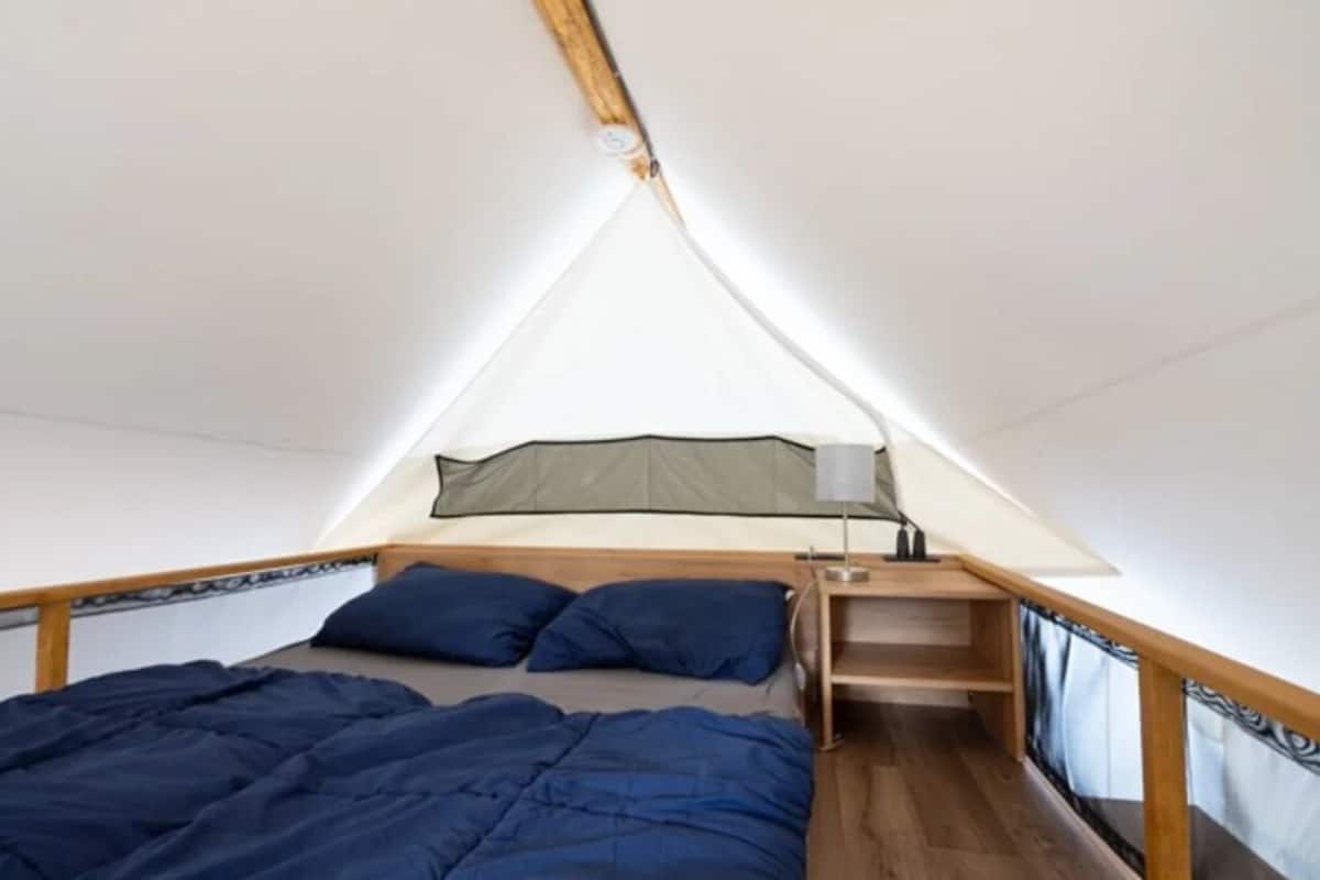 A triangular tent-style room with a bed, a shelf, and a window.