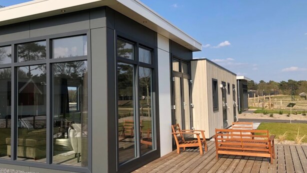 A modern building with large glass windows and a wooden deck with outdoor furniture.