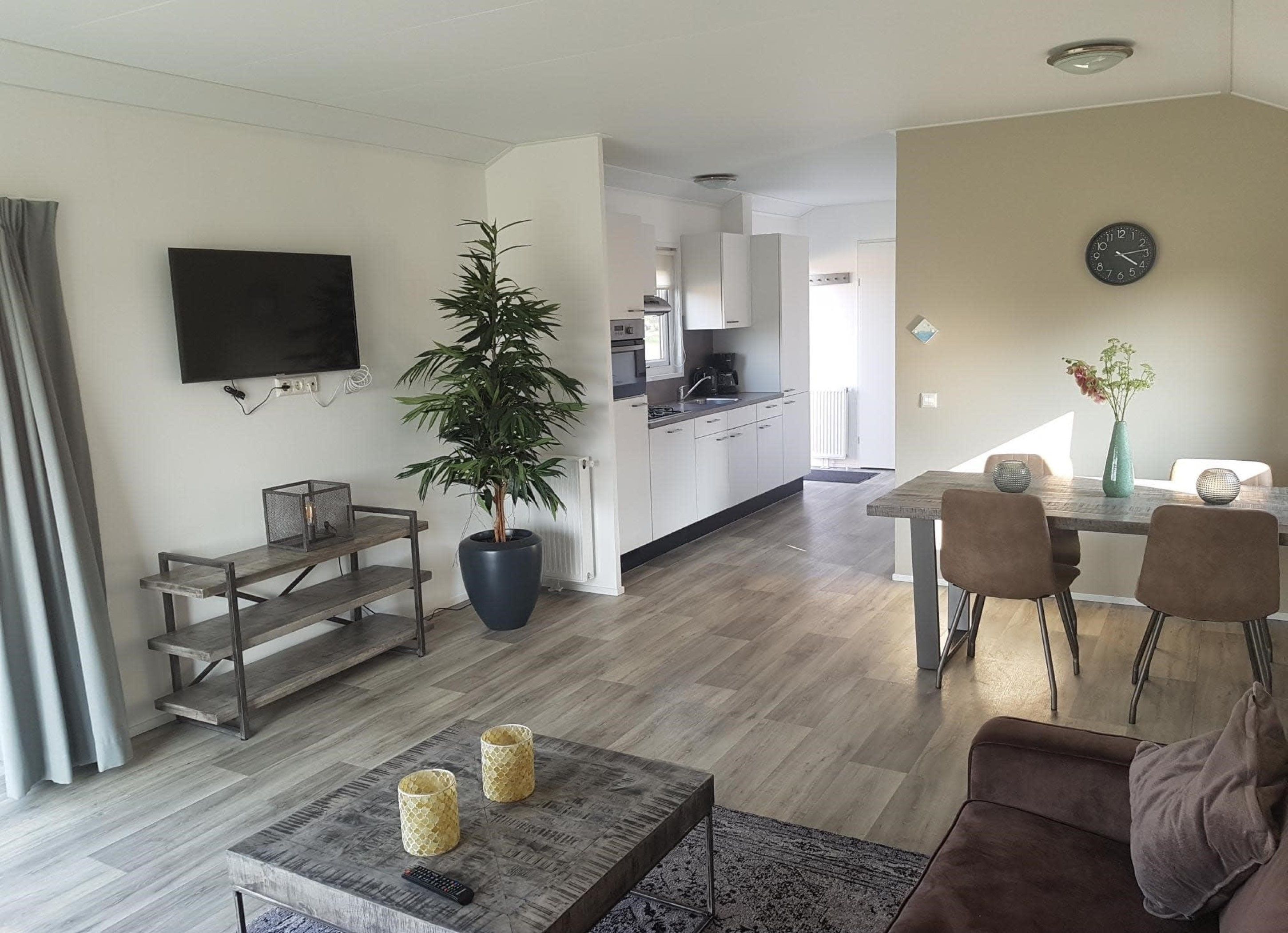 A modern living room with a flat-screen TV, a large potted plant, a wooden coffee table, and a dining area with a table and chairs.
