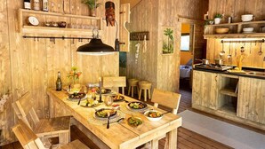 A rustic wooden dining area with a long table set for a meal, wooden chairs, and a hanging light fixture.