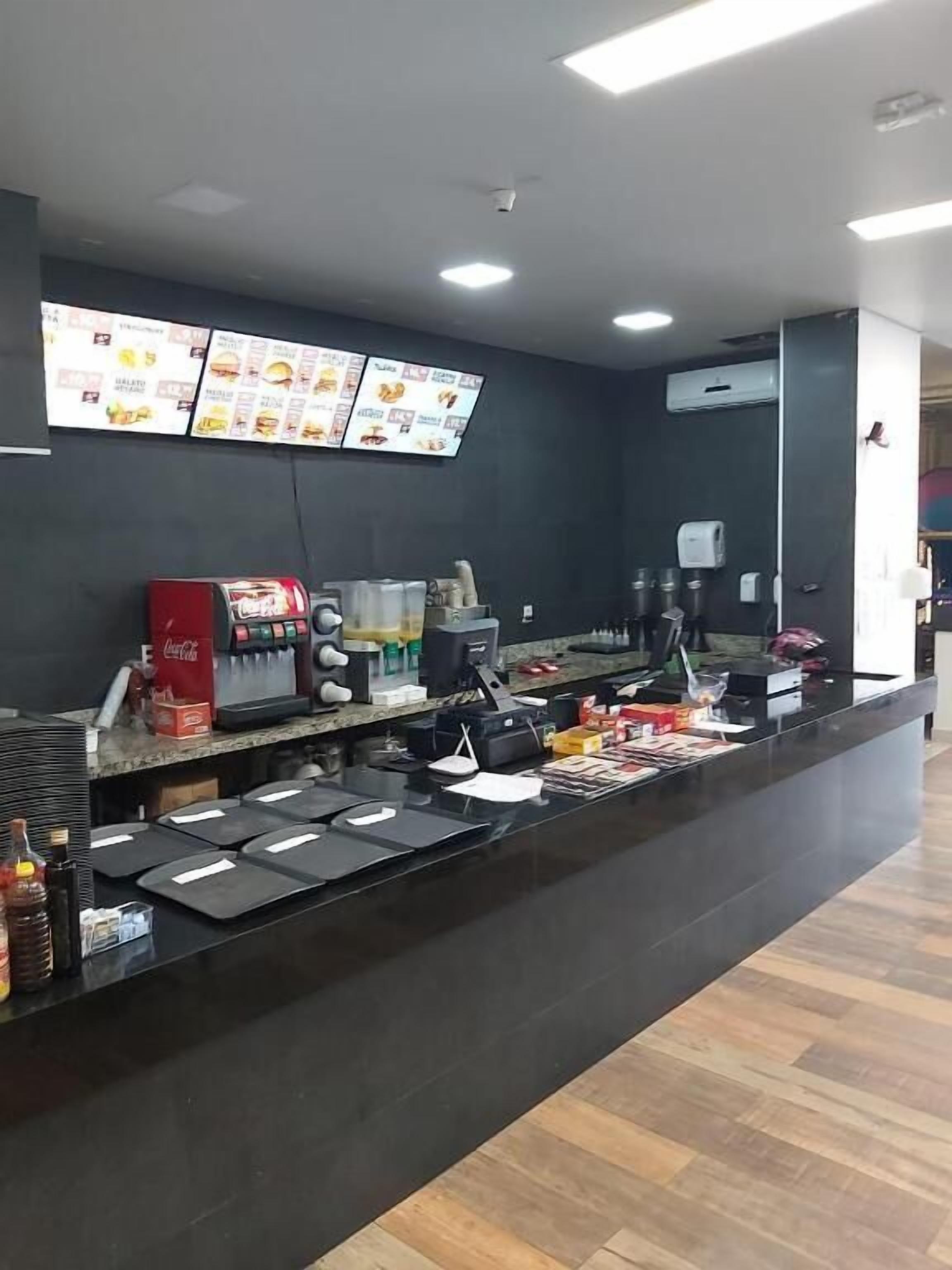 A counter with a menu board, a Coca-Cola dispenser, and a coffee machine.