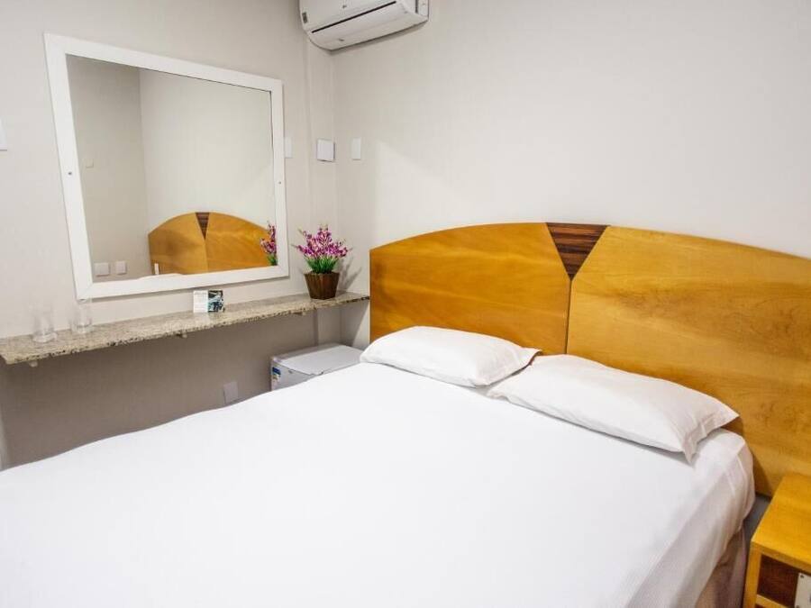 Habitación de hotel con cama, mesita de noche, espejo y una pequeña planta en maceta.