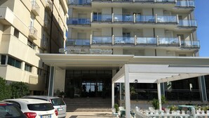 A multi-story hotel with balconies, a covered entrance, and outdoor seating. - Hotel Excelsior (Cattolica)