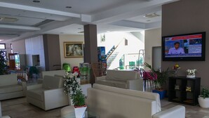 A modern hotel lobby with comfortable seating, a TV displaying news, and a staircase leading to an outdoor area. - Hotel Excelsior (Cattolica)
