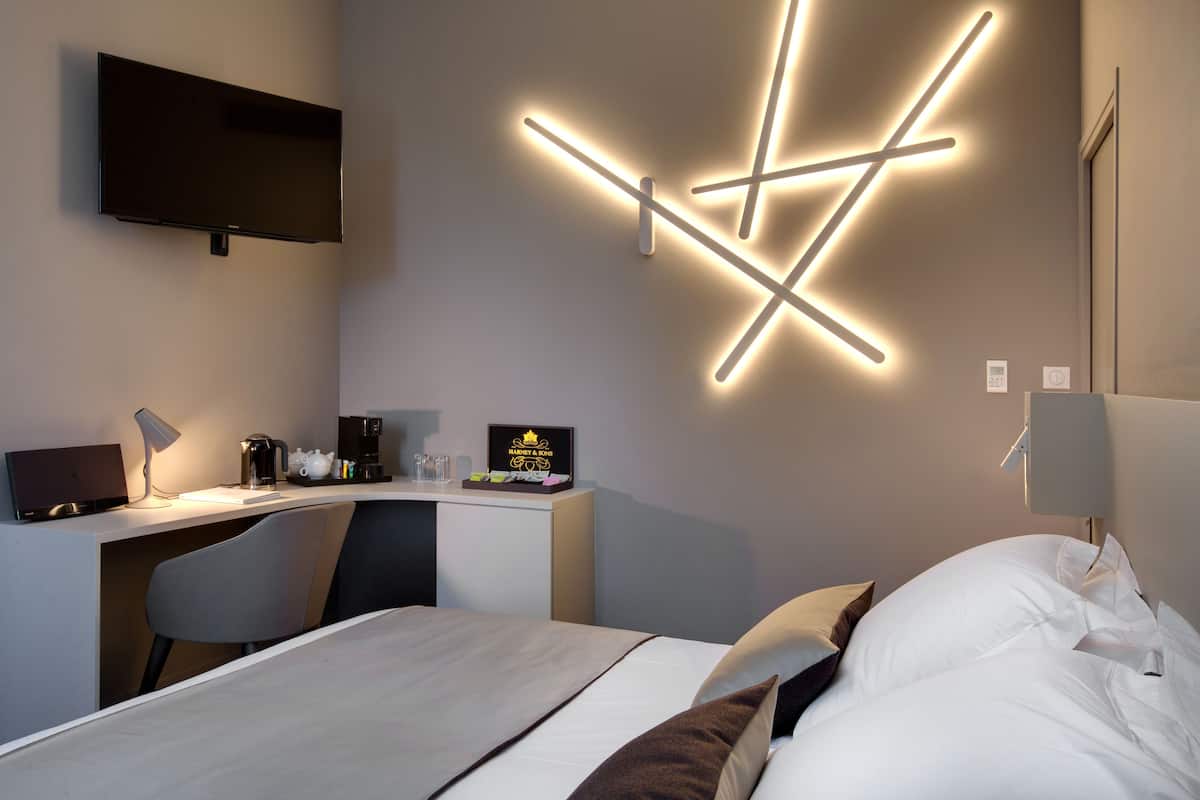 A modern hotel room with a bed, desk, and TV.