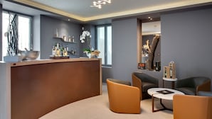 A modern reception area with a curved wooden counter, seating with orange and black cushions, and a decorative vase with white flowers. - Hotel Mas de Boudan (Nîmes)
