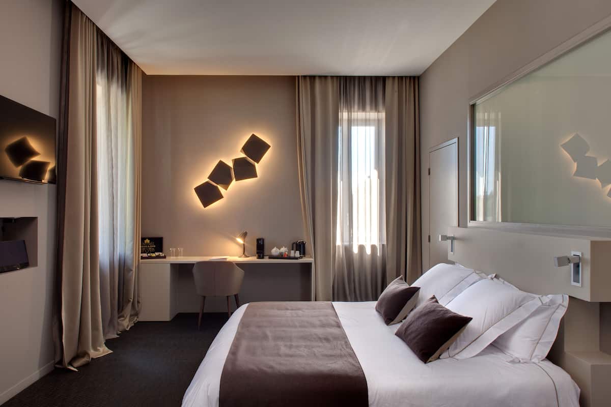 A hotel room with a bed, desk, chair, and a large mirror.