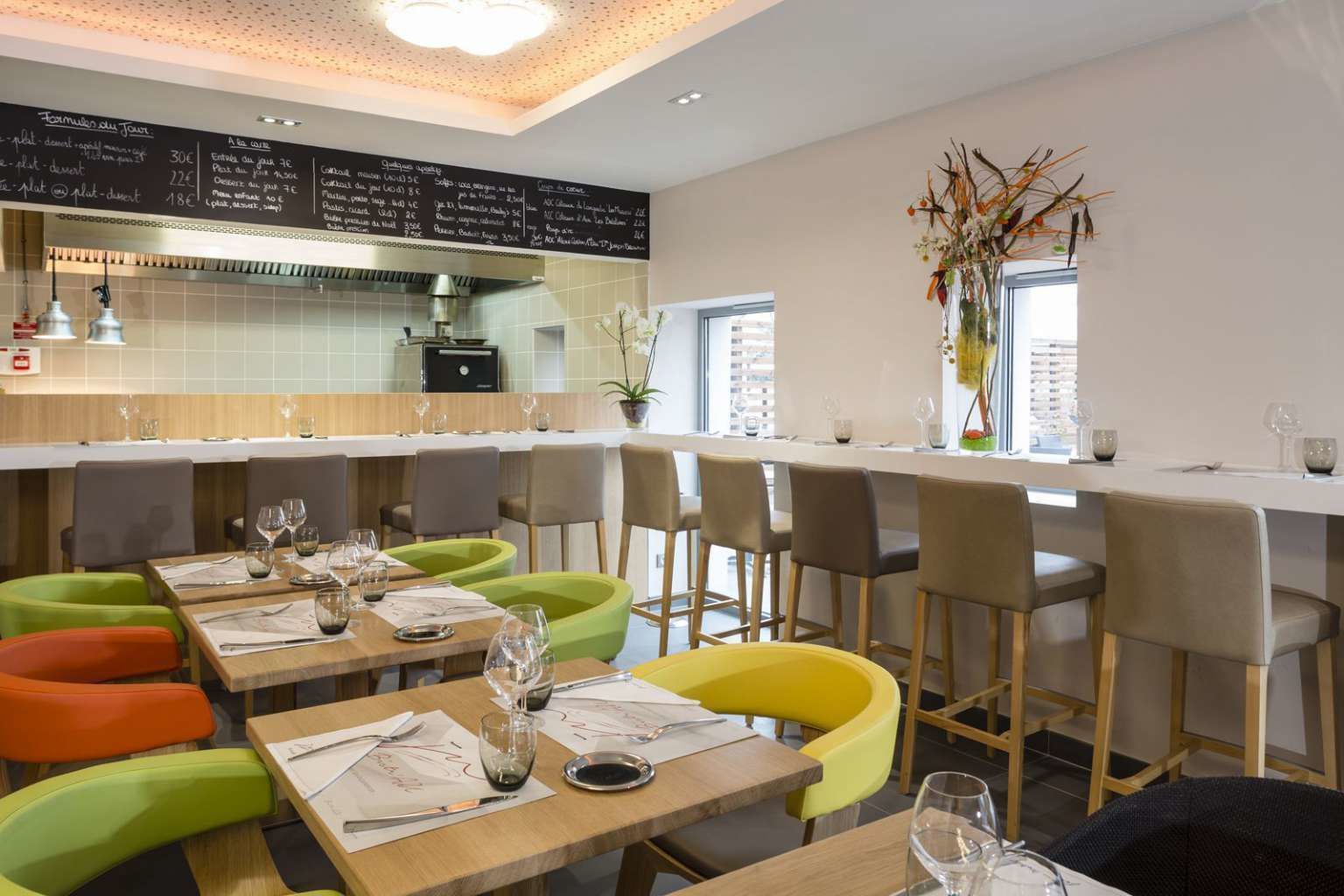 Un restaurante moderno con una barra larga y varias zonas de estar, incluyendo sillas coloridas y un espacio para bar.