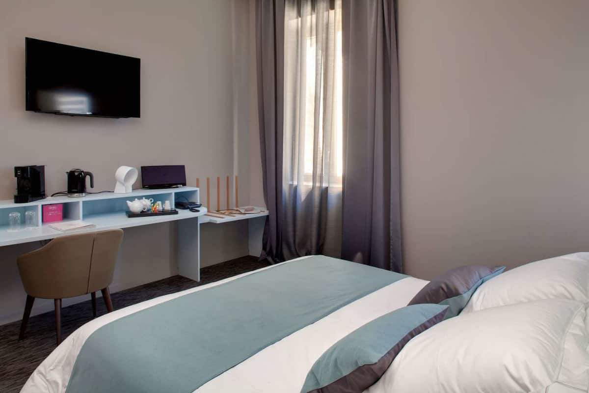 A hotel room with a bed, a desk with a laptop, a coffee maker, and a TV.