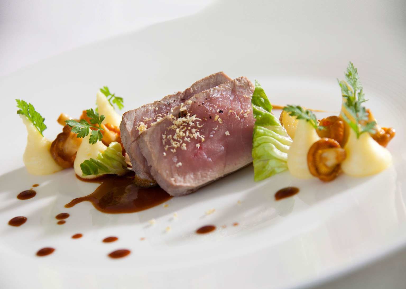 A white plate with a piece of meat, vegetables, and sauce.