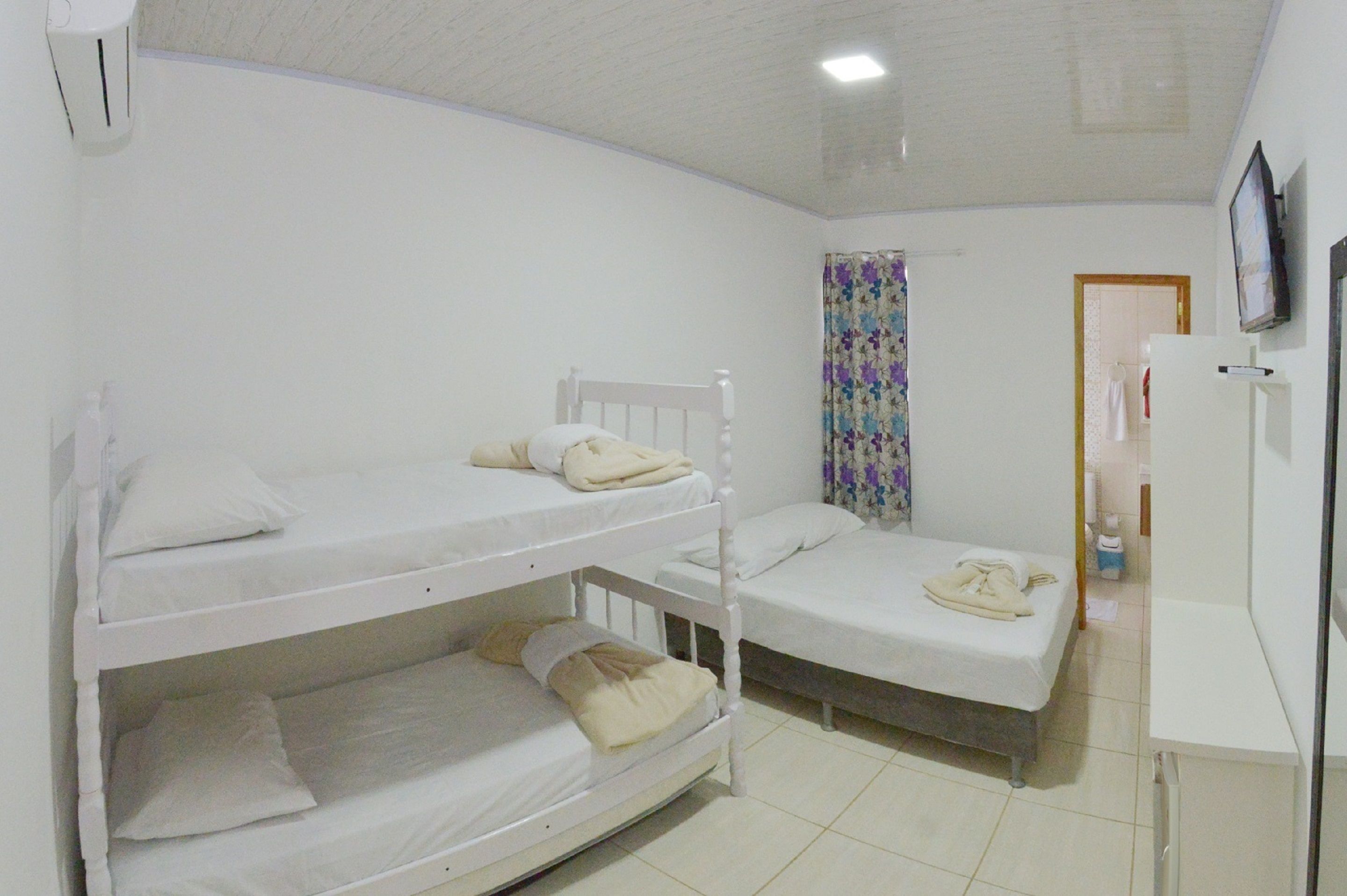 A room with bunk beds, a television on the wall, and a door leading to another room.