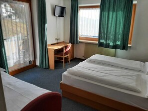Hotellihuone, jossa on sänky, työpöytä, tuoli, televisio ja ikkuna, jossa on verhot.