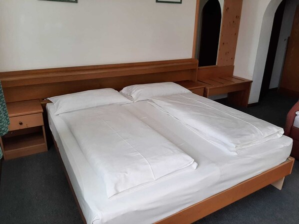A double bed with white linens, wooden headboard, bedside tables, and a small drawer. - Pension Marianne (Rio di Pusteria)