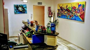 A reception area with a desk, chairs, artwork on the walls, and a sign indicating the exit. - Torremolinos Hostel (Torremolinos)