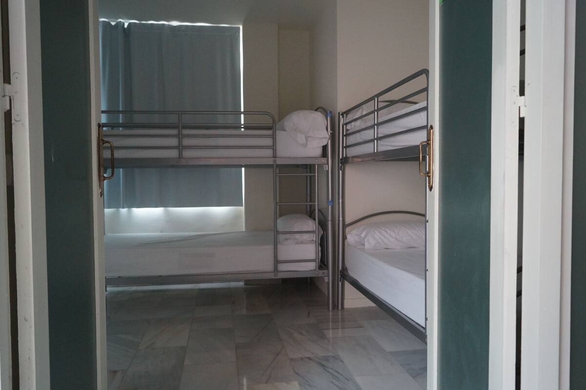 A room with bunk beds, a window with curtains, and a tiled floor.