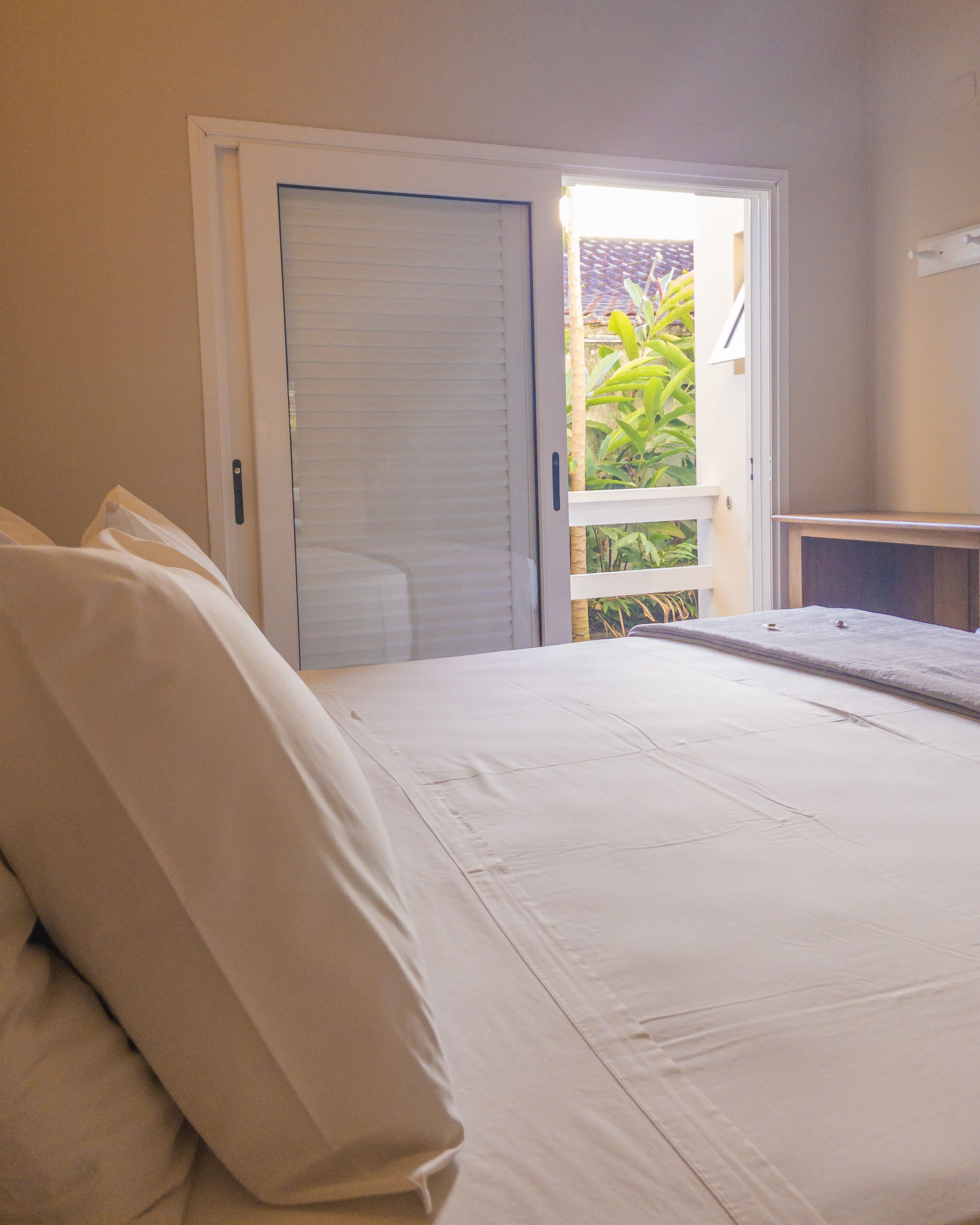 Un dormitorio con cama, puerta y vistas al verde exterior.