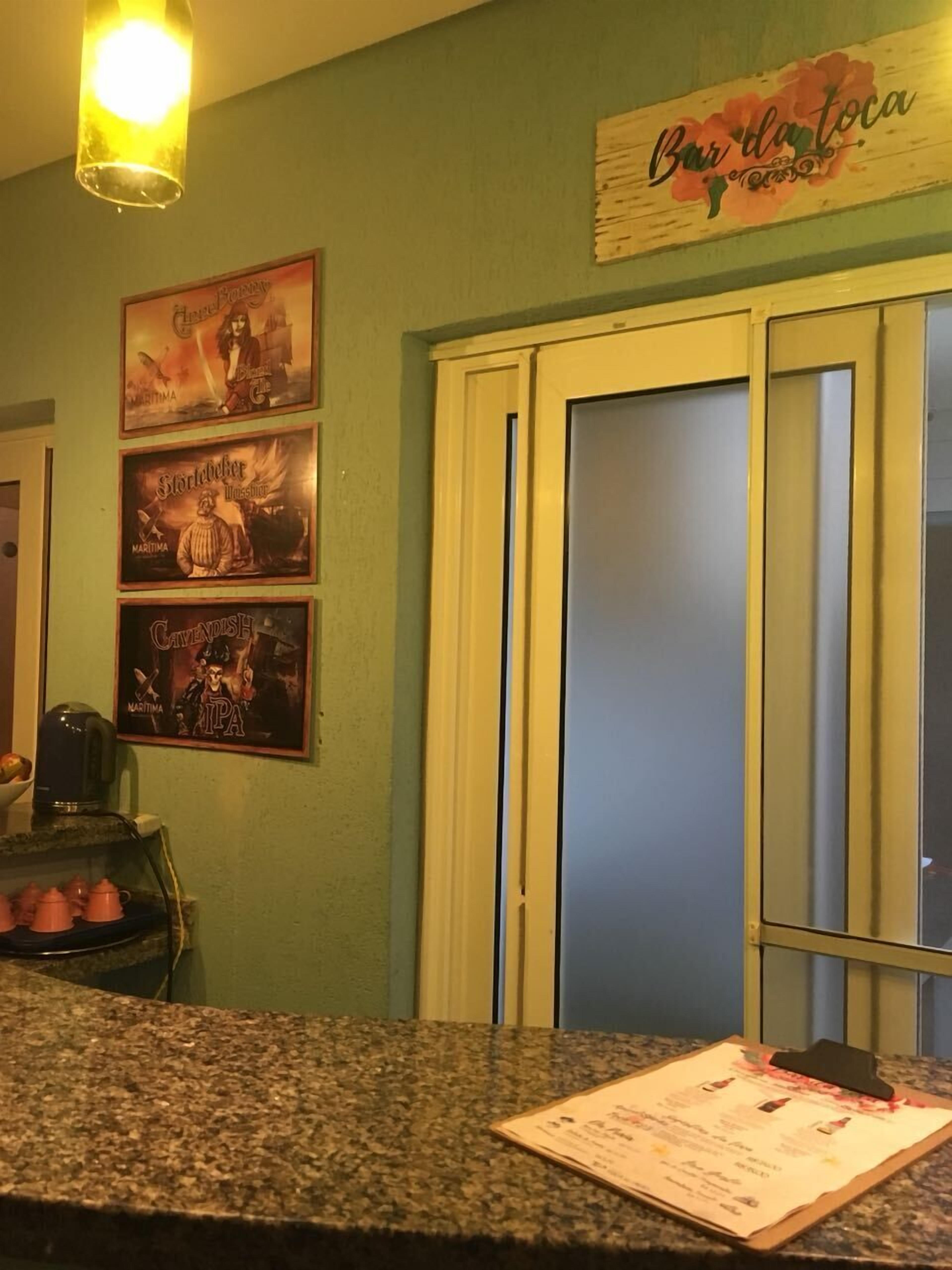 Una cocina con encimera de granito, una cafetera y un menú sobre la encimera. Hay tres carteles enmarcados en la pared y una puerta con un cartel encima.
