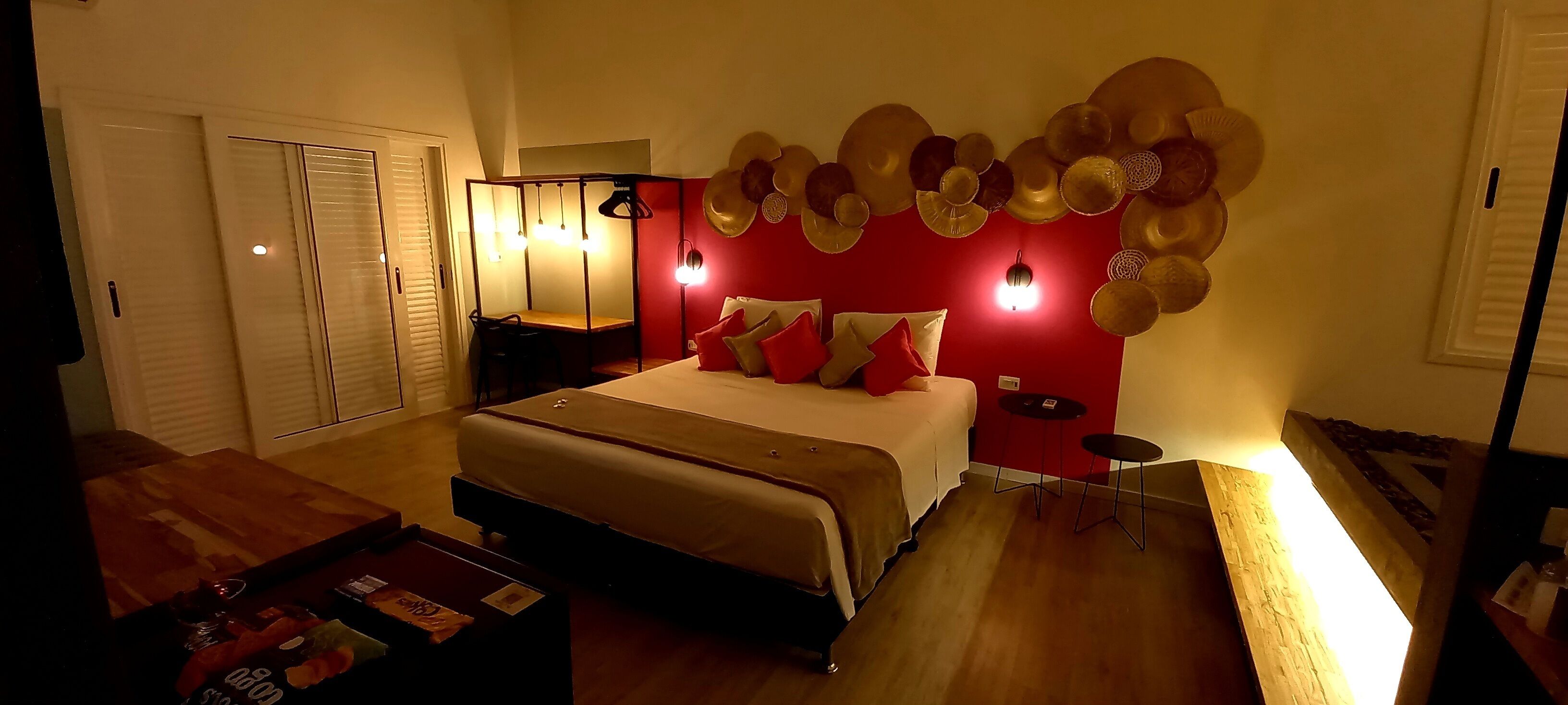 Un dormitorio con cama, mesitas de noche, una mesa de centro de madera y una pared decorativa de color rojo con platos ornamentales.