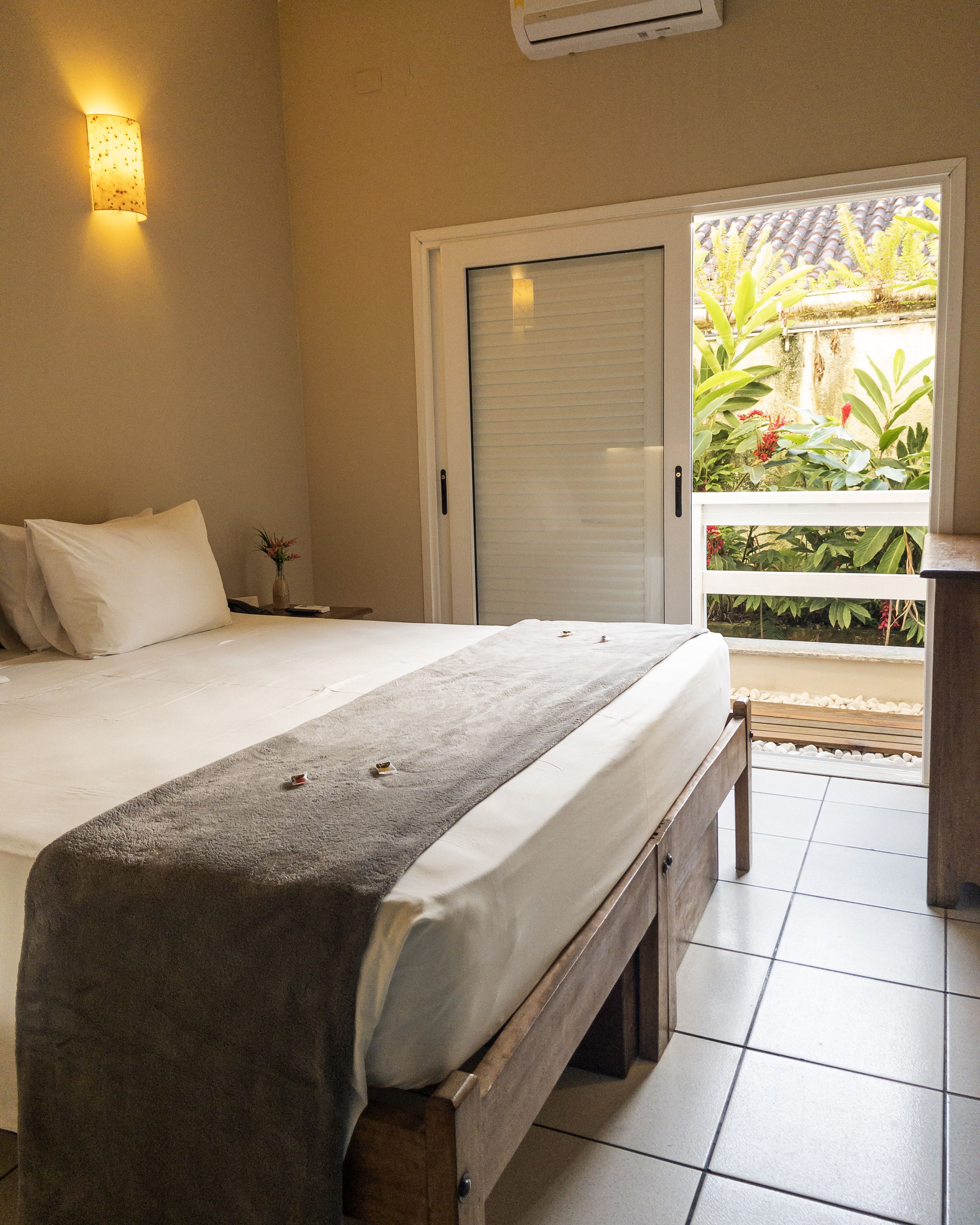 Un dormitorio con cama, mesita de noche, ventana con vistas a zonas verdes y equipo de aire acondicionado.