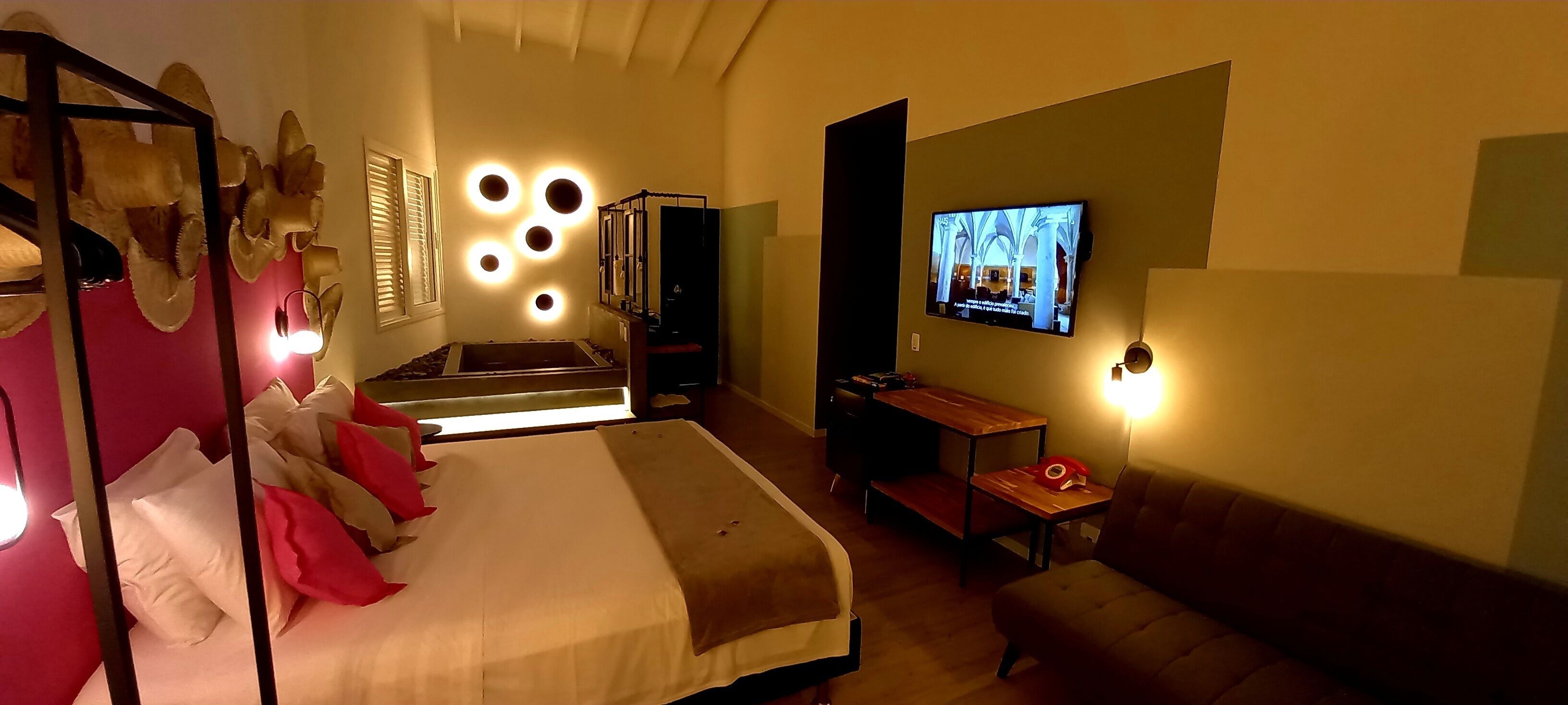 A hotel room with a bed, a desk, a television, and a wall-mounted light fixture.