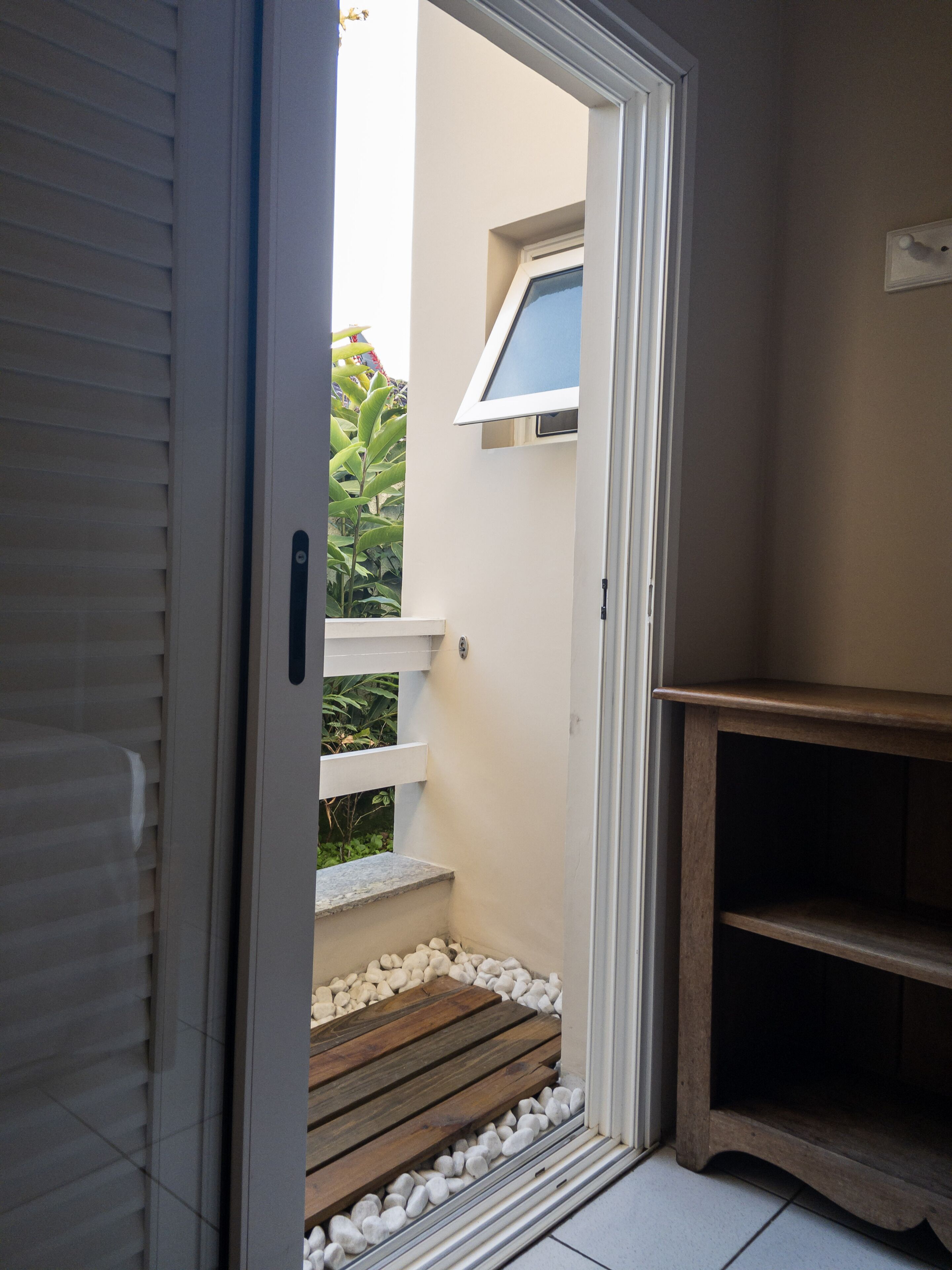 Una puerta que da a un balcón con un banco de madera y un pequeño jardín con guijarros blancos.