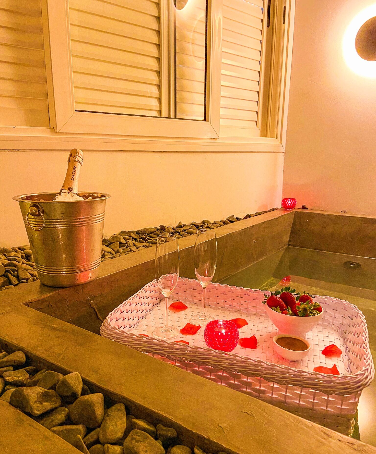 Un bain à remous parsemé de pétales de rose, un verre de vin et une bouteille de champagne.
