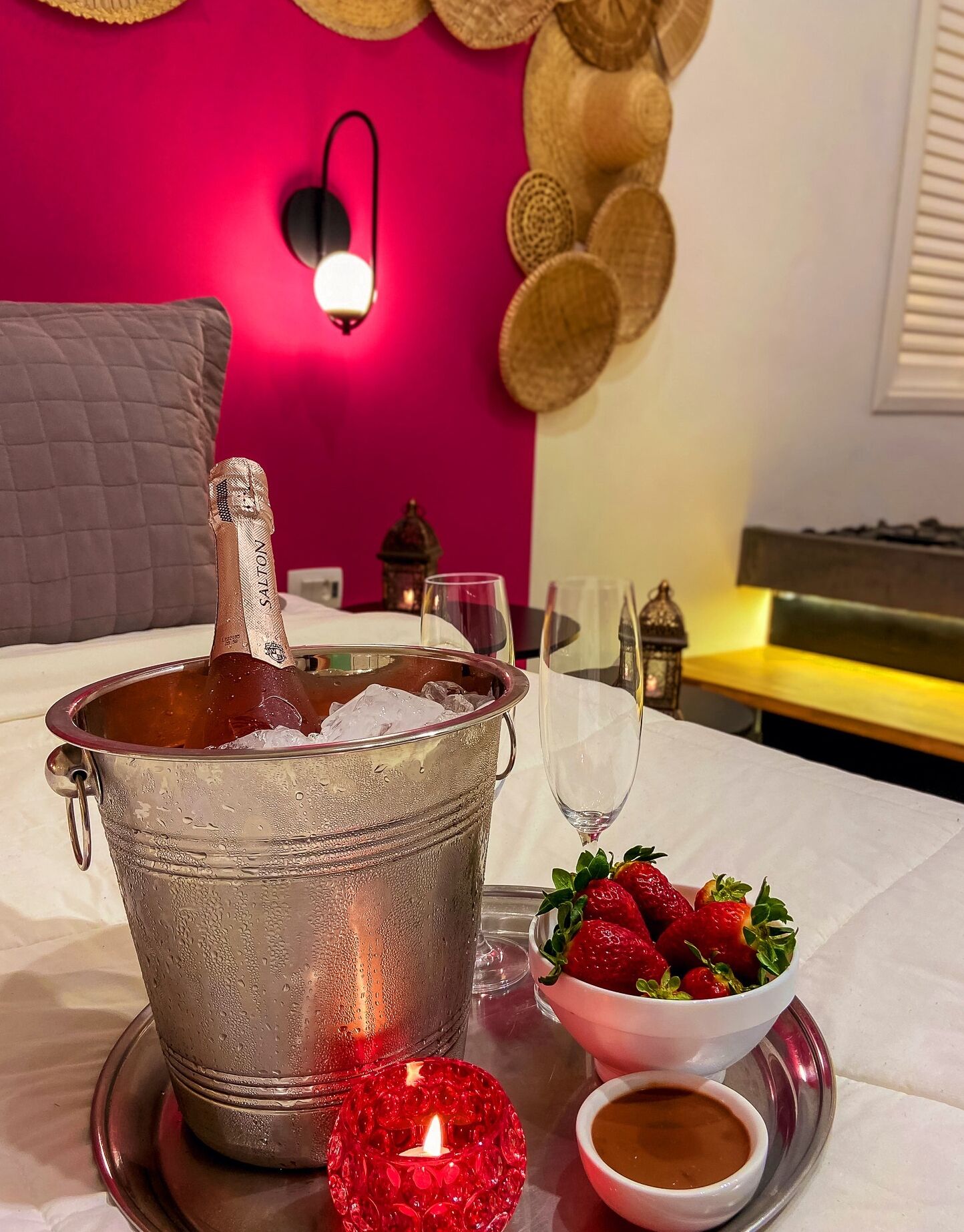 A dining table with a metal bucket of ice, a glass of water, a bowl of strawberries, and a candle.