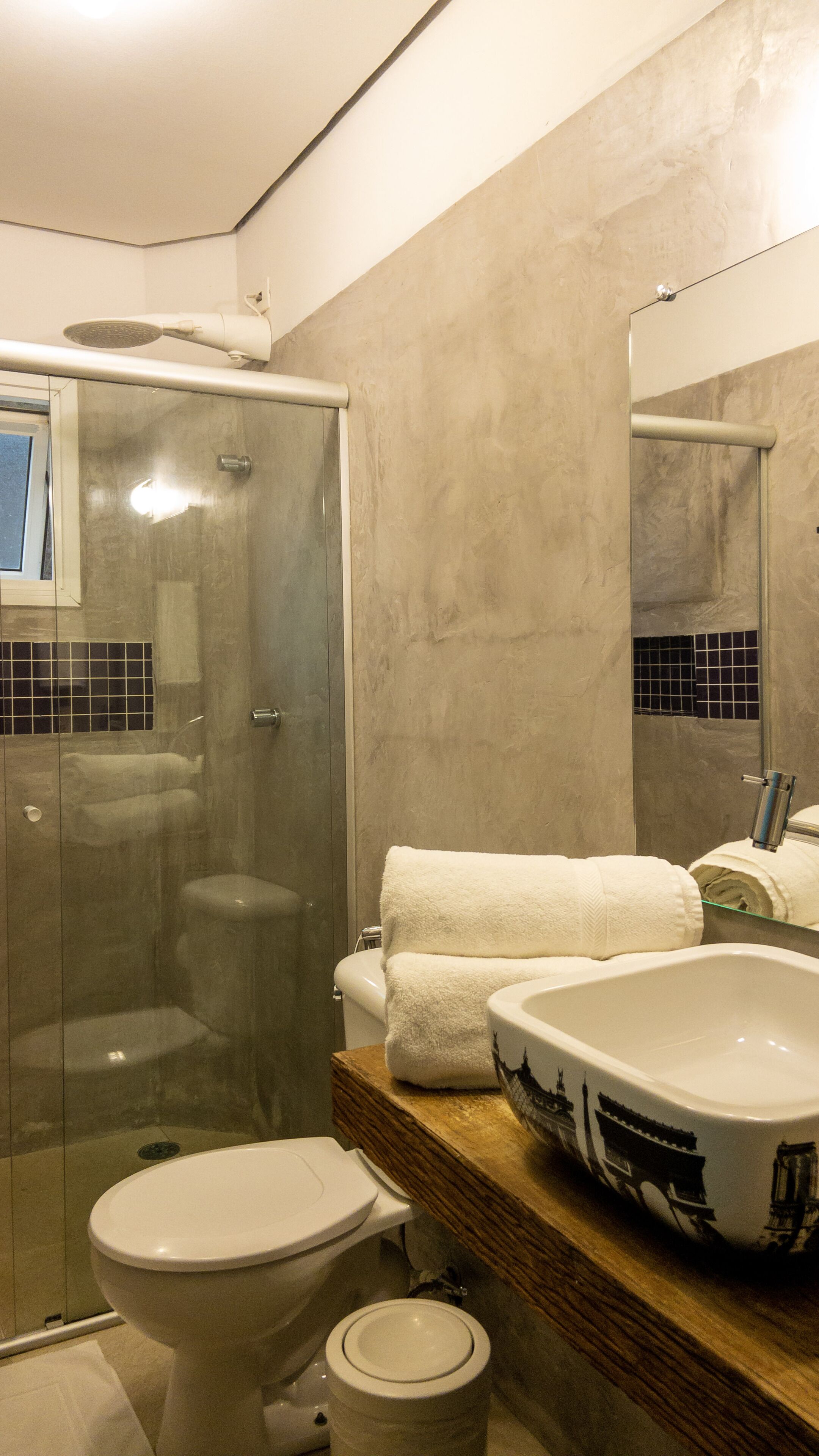 A modern bathroom with a glass-enclosed shower, a toilet, and a sink with decorative tiles.