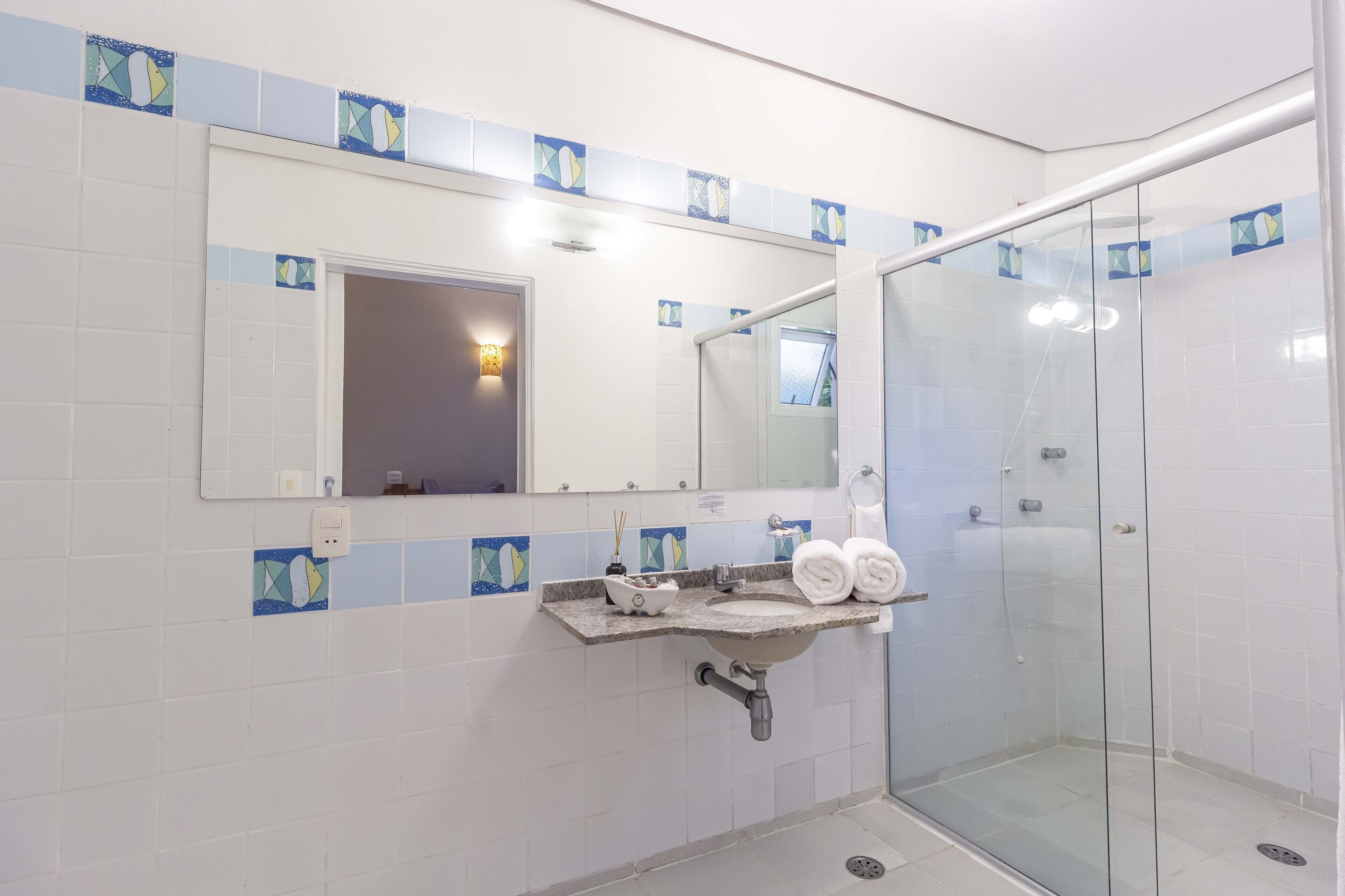 A bathroom with a glass shower enclosure, a sink with a marble countertop, and a mirror above the sink.