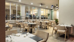 Un amplio comedor interior con varias mesas y sillas de mimbre, ventanas grandes y luces de techo.