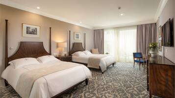 A hotel room with two beds, a desk, a chair, and a TV.