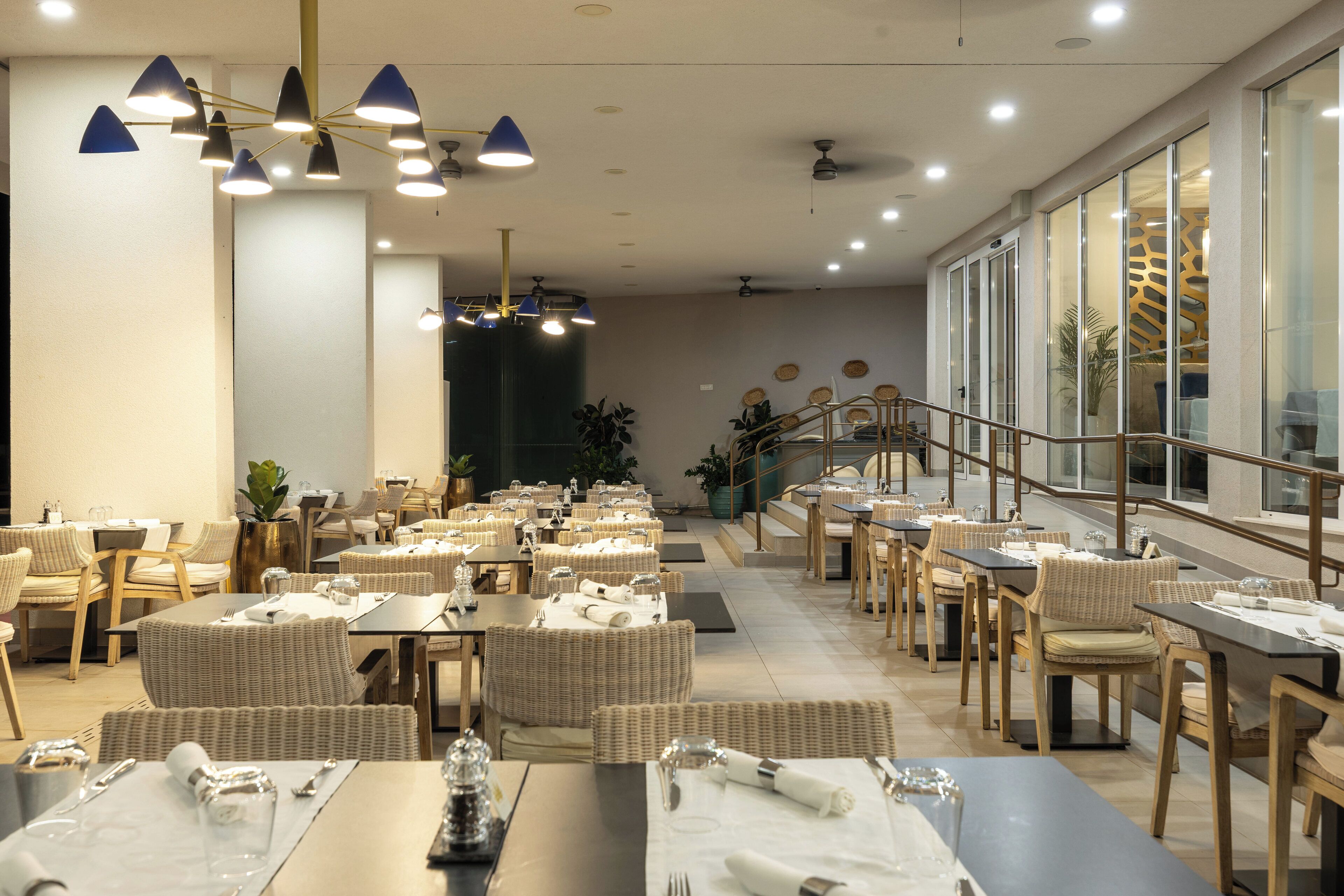 A restaurant with multiple tables and chairs, a staircase, and large windows.