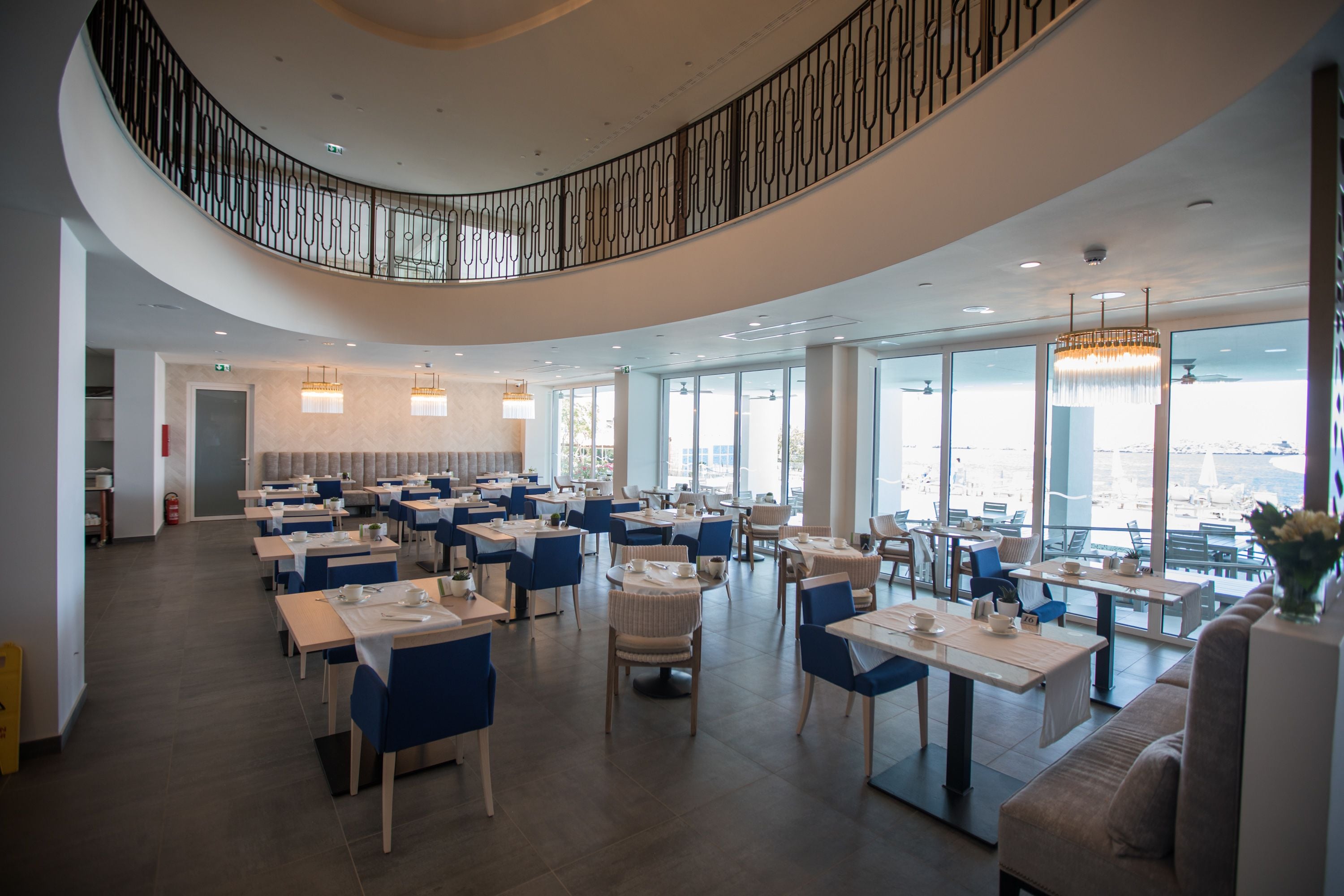 Un espace de restauration moderne doté de plusieurs tables et chaises, d’un plafond incurvé et de grandes fenêtres offrant une vue panoramique.