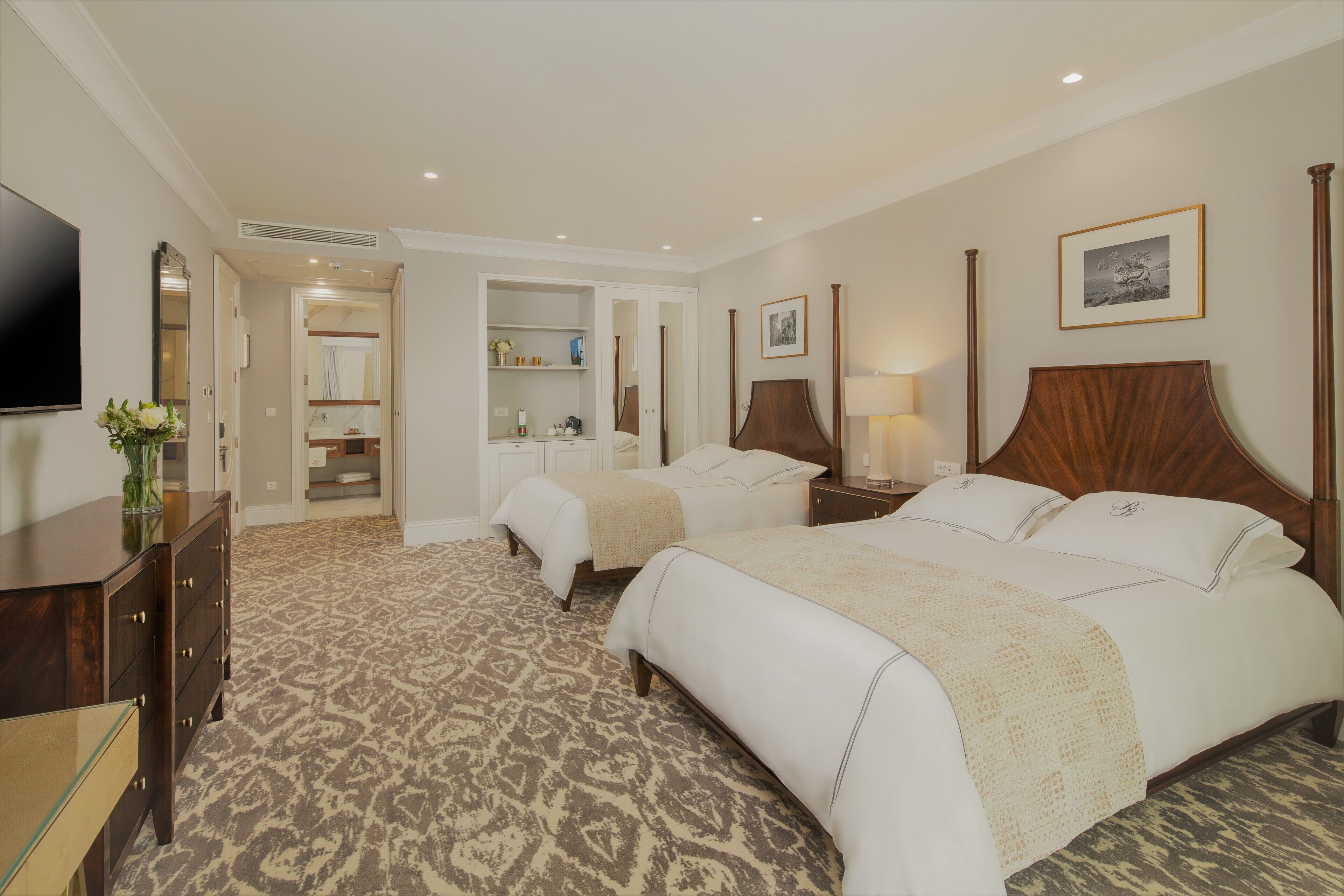 Una habitación de hotel con dos camas, un televisor, un aparador y un vestidor.