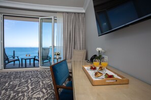 A hotel room with a balcony, a dining table with breakfast, and a TV mounted on the wall.