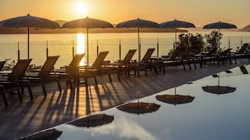 Área à beira da piscina com espreguiçadeiras e guarda-sóis, com vista para um corpo de água.