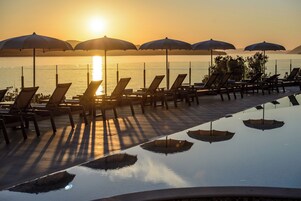 Área à beira da piscina com espreguiçadeiras e guarda-sóis, com vista para um corpo de água.