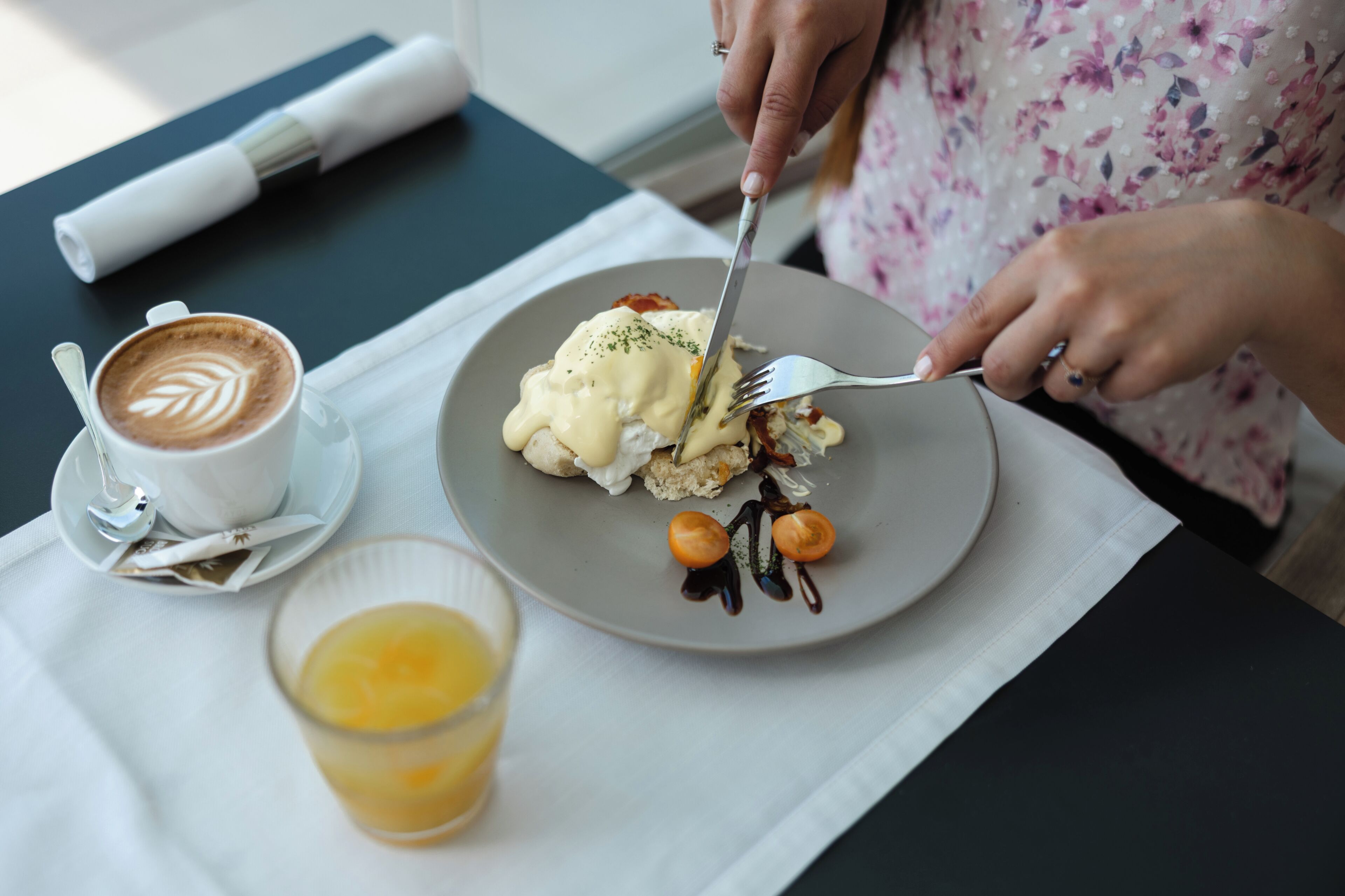 Una persona comiendo en una mesa con un plato de comida, una taza de café y un vaso de jugo de naranja.