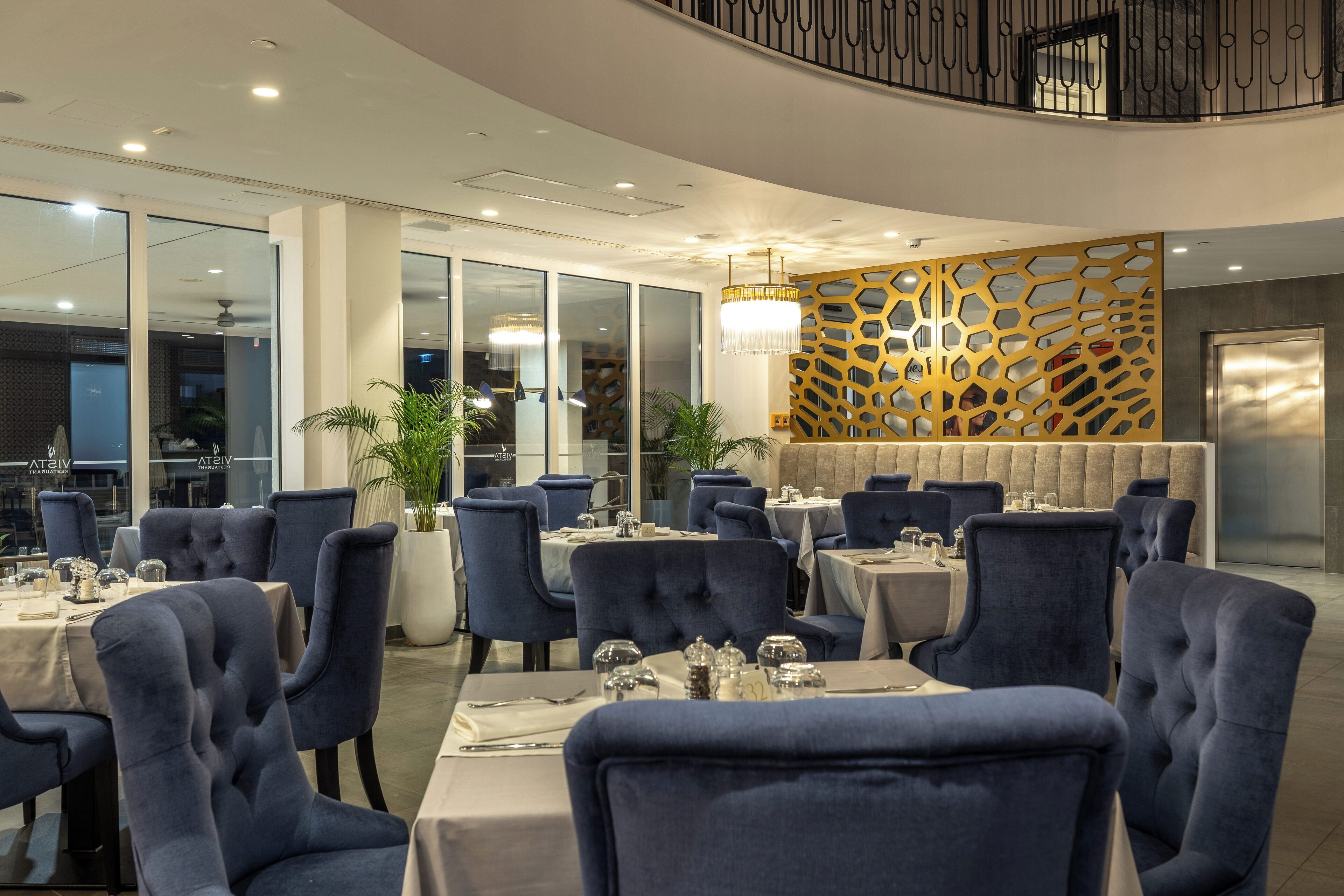 A restaurant with round tables and blue upholstered chairs, a decorative wall, and a chandelier.