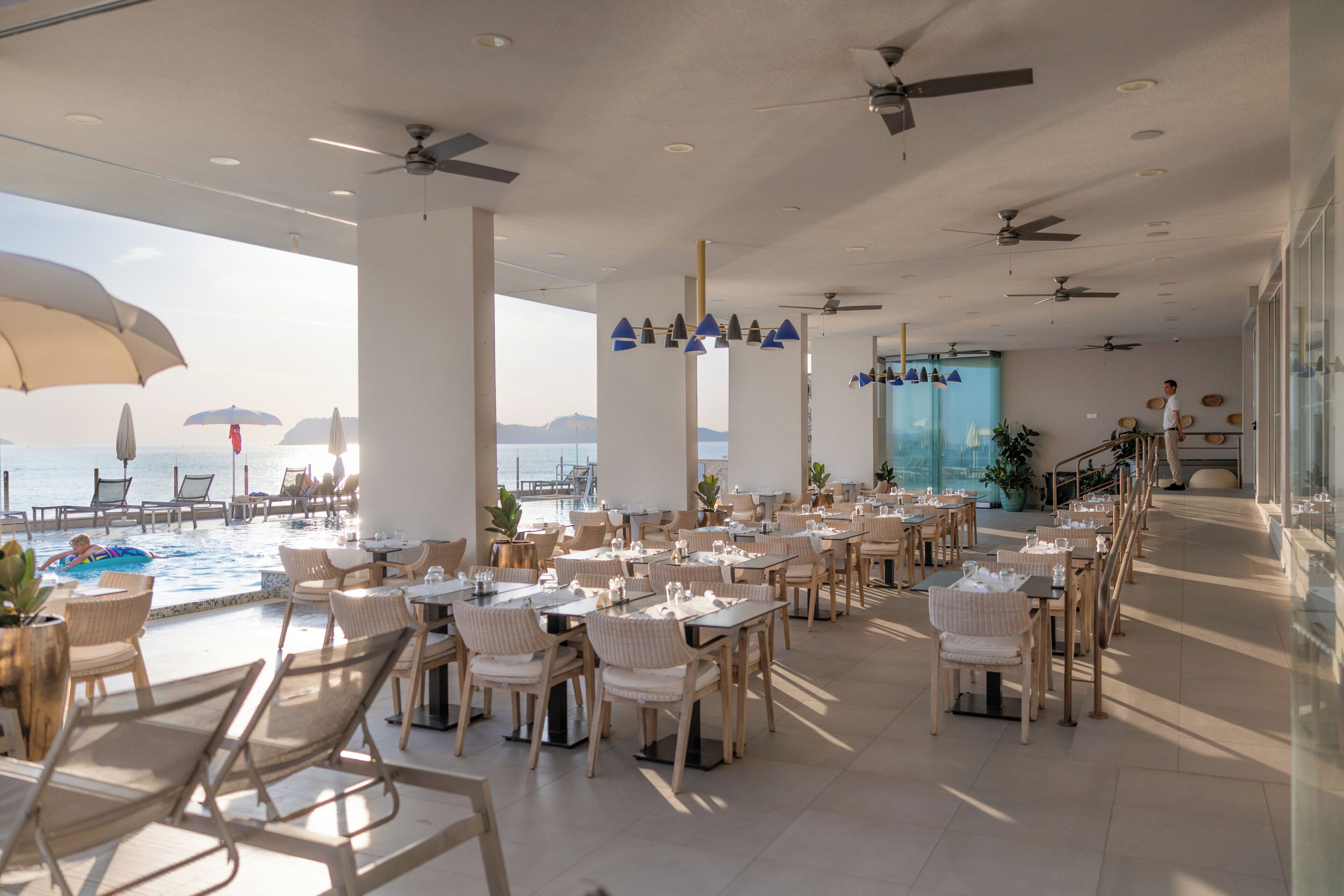 Un vaste espace extérieur aménagé pour les repas, avec des tables et des chaises, une piscine et une vue sur la mer.