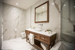 Un baño moderno con pared de mármol, tocador de madera, un espejo grande y cabina de ducha de vidrio.